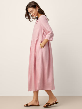Linen maxi dress by LINTICO with crescent neckline, decorative buttons, waist pleats, and flowing silhouette.